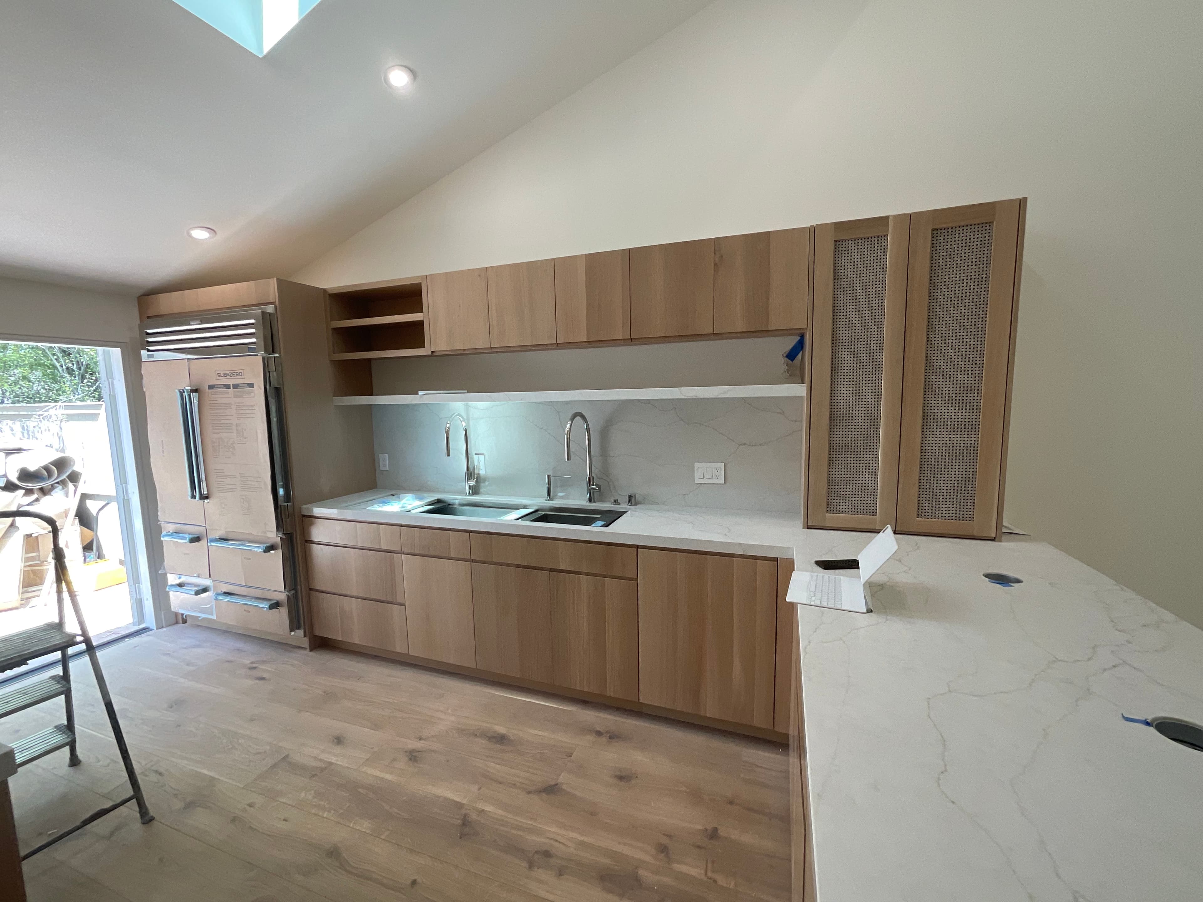 Modern kitchen with light wood cabinets, white marble countertops, double sink, and vaulted ceiling.